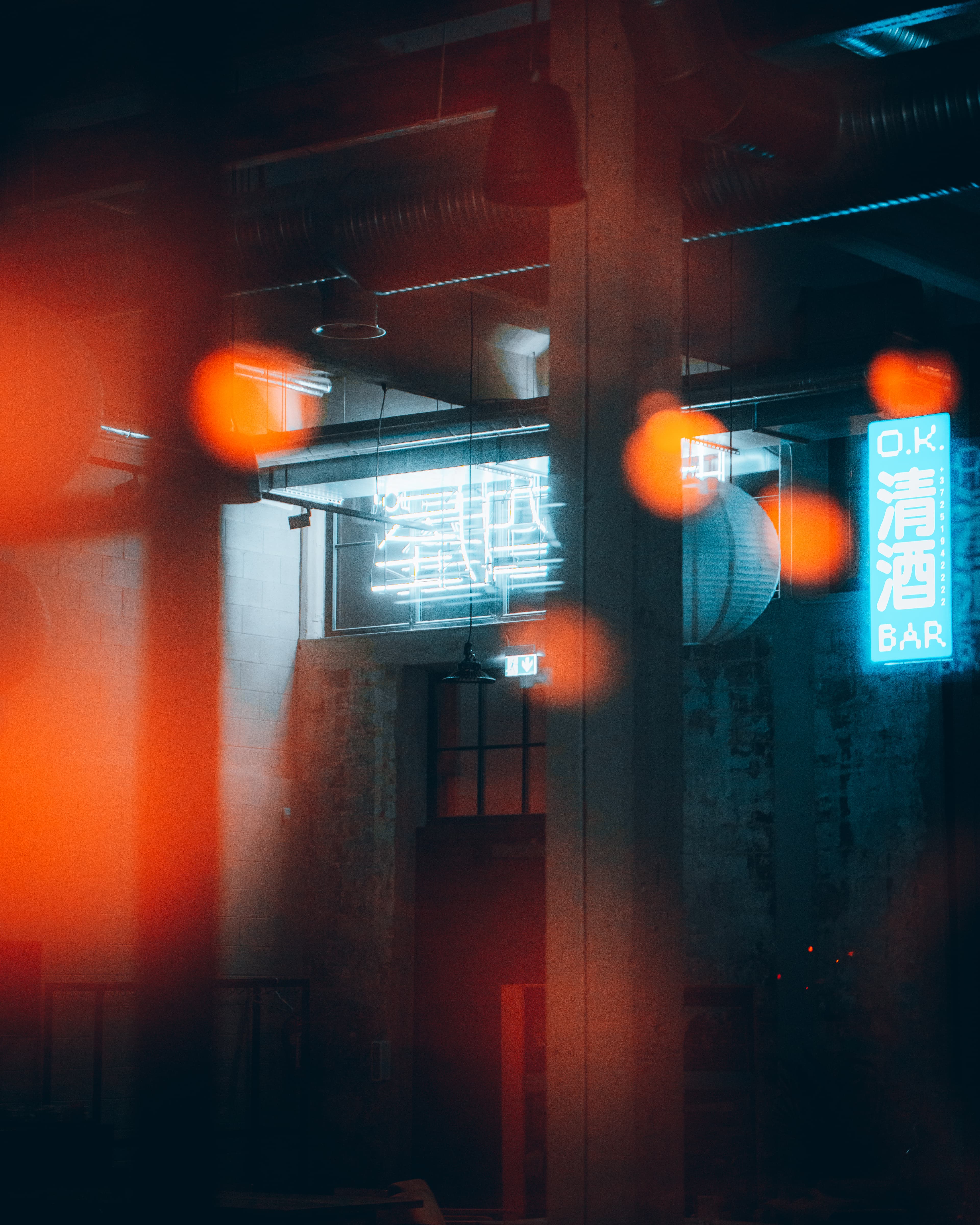 An industrial interior features blue street signs in Japanese, captured from the street through a window, creating orange lens flares reflecting from the lights.